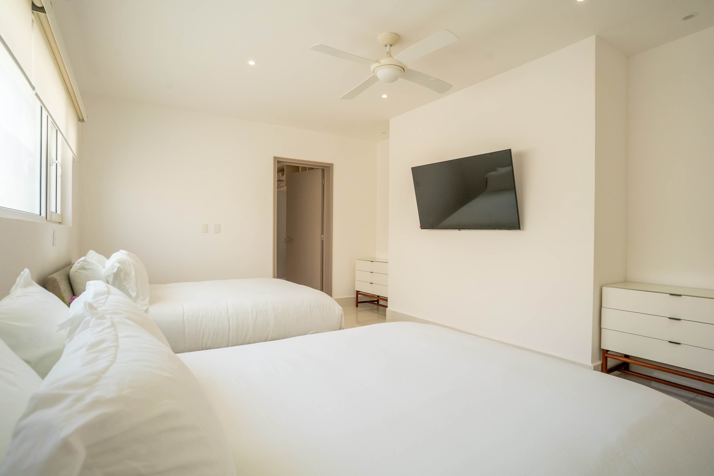 A white bedroom with two beds, a TV, and a dresser.