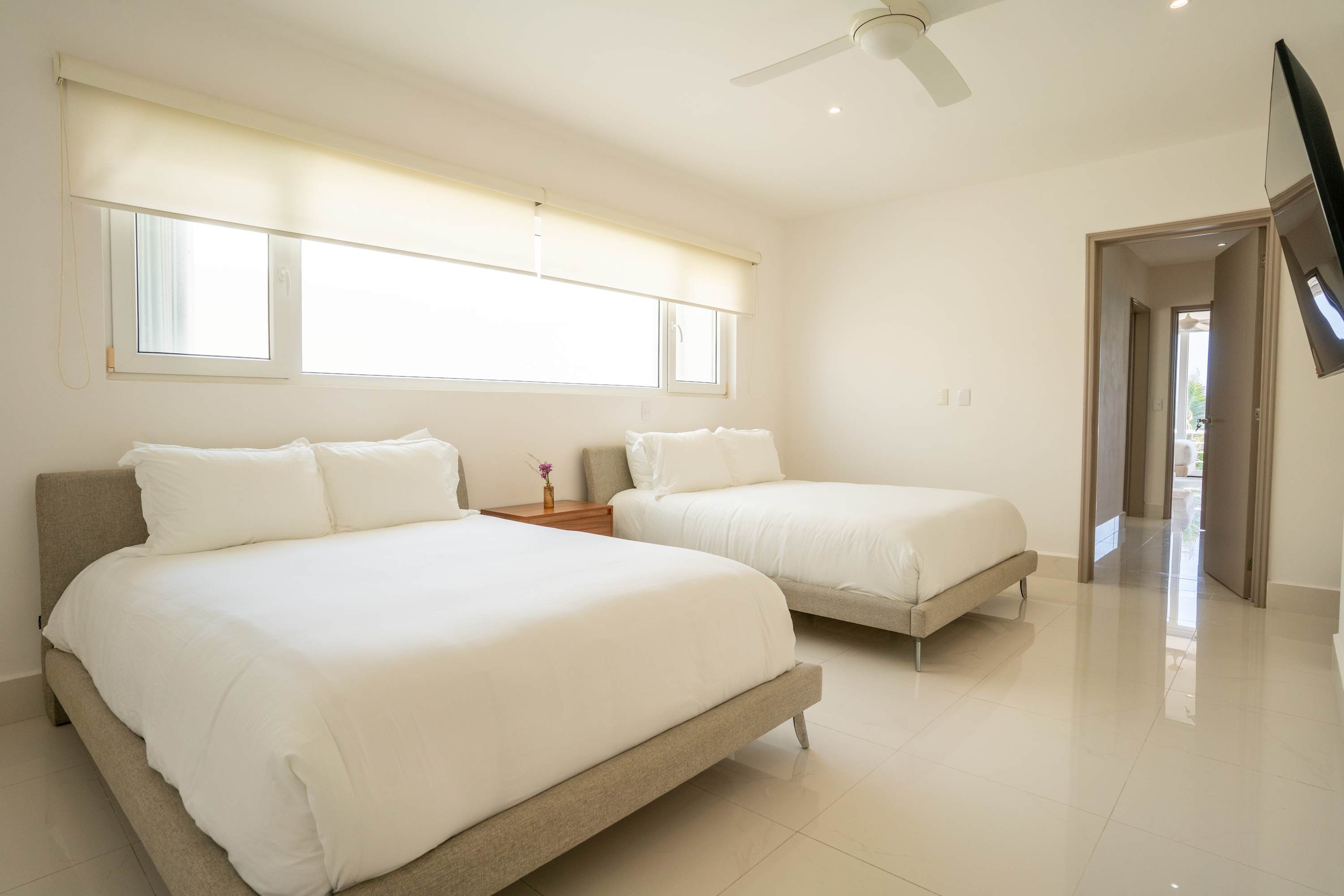 A bedroom with two beds, a fan, and a TV.
