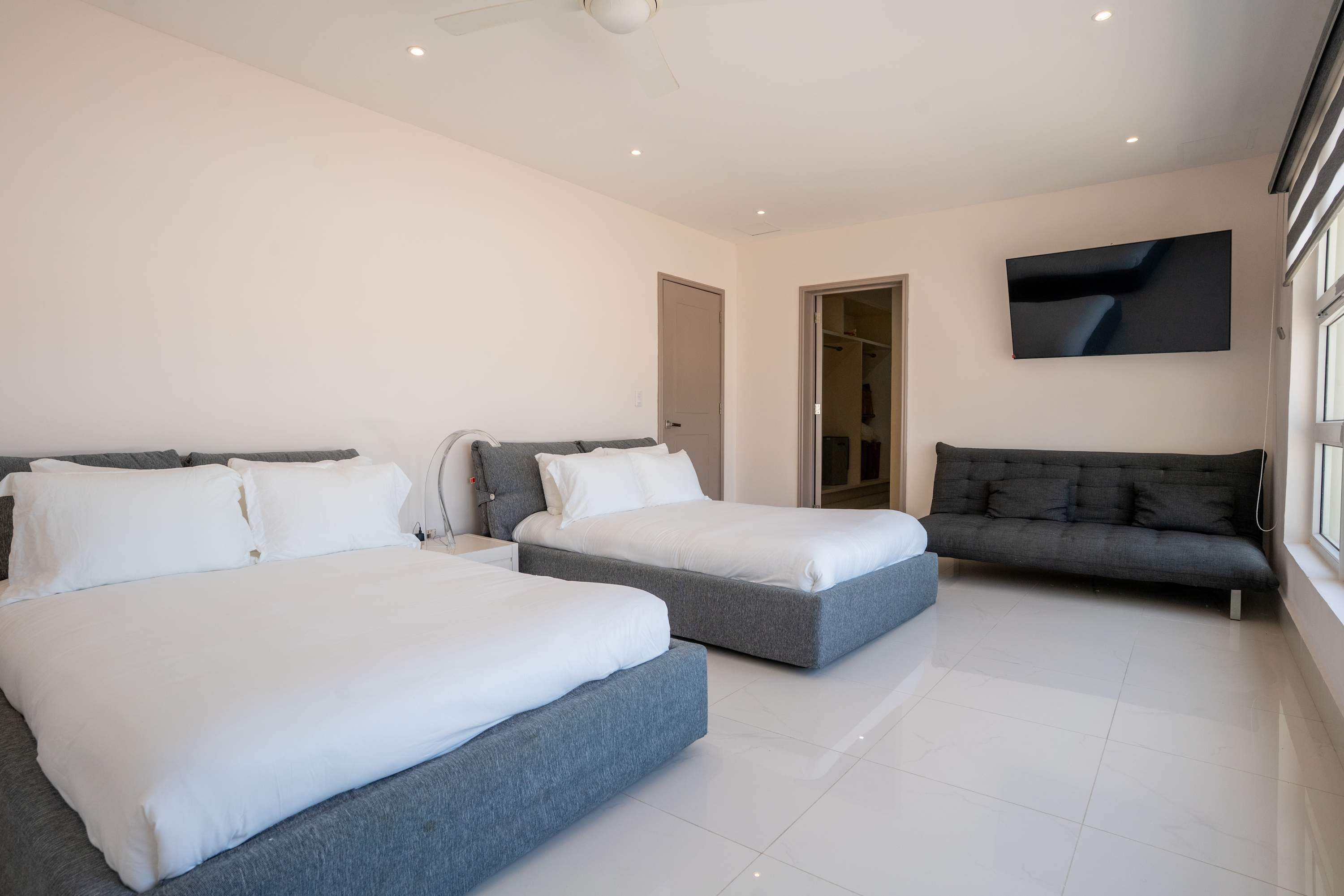 Modern bedroom with two beds, a sofa, a TV, and a closet.