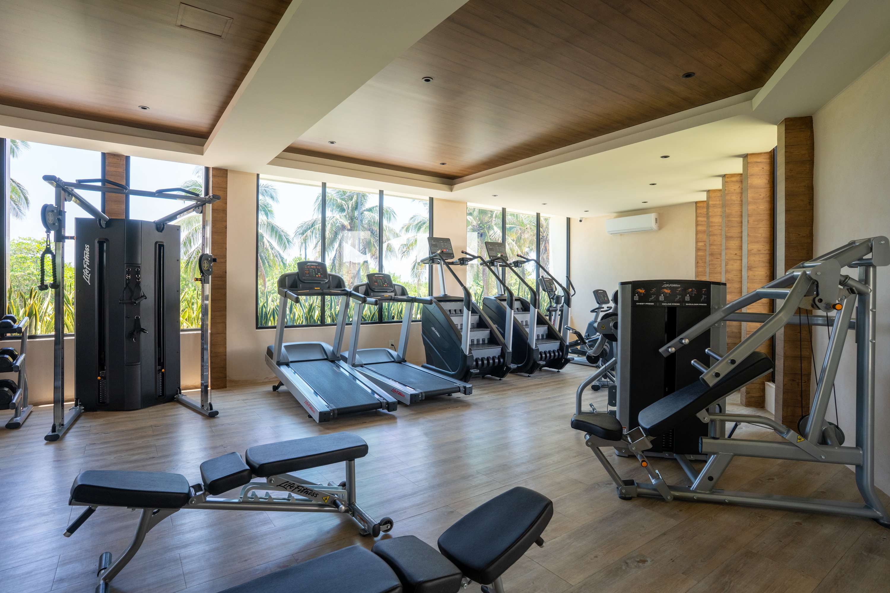 A modern gym with treadmills, stair climbers, and weight machines, featuring large windows overlooki