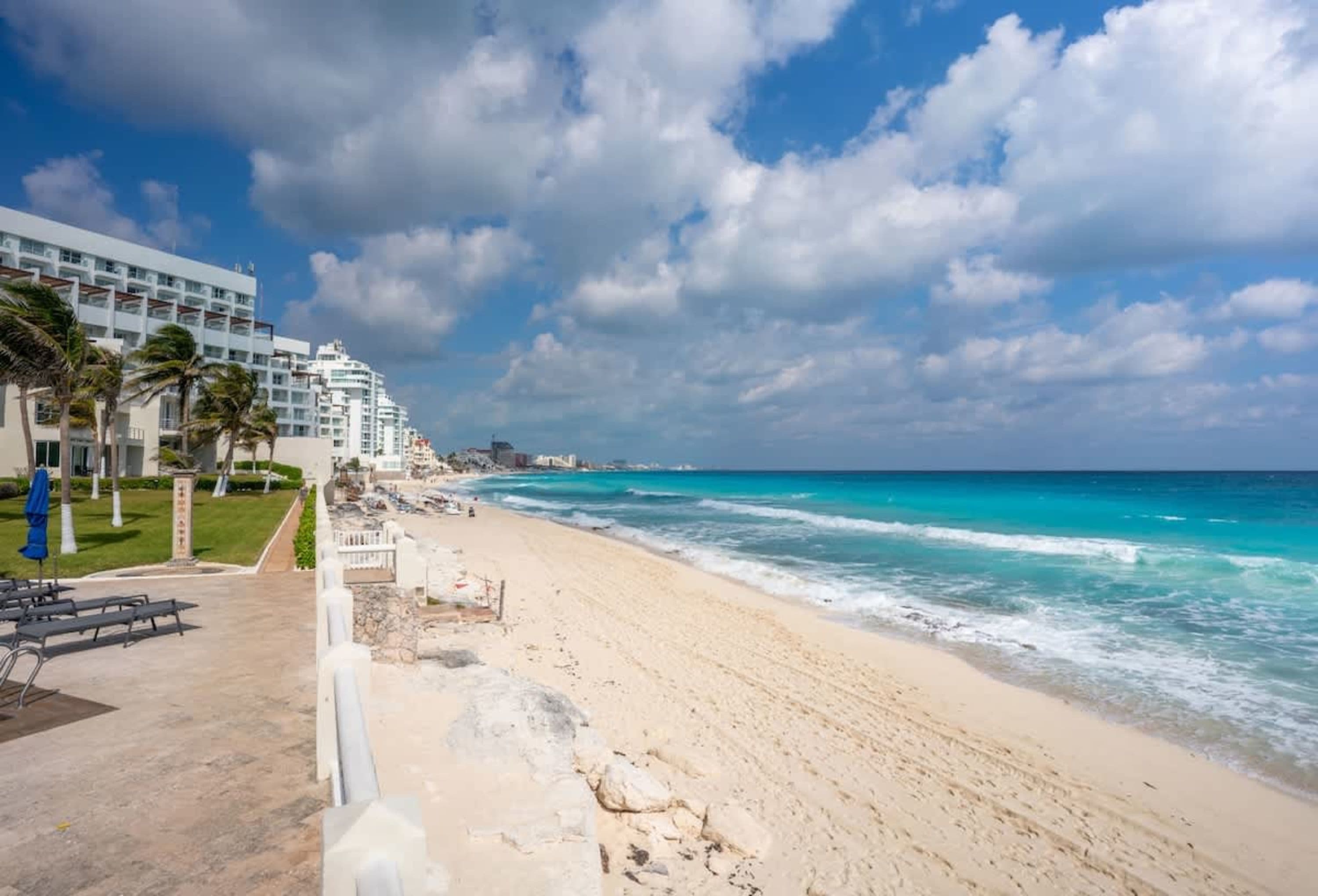 A beautiful beach with turquoise water, white sand, and tall hotels under a cloudy sky.