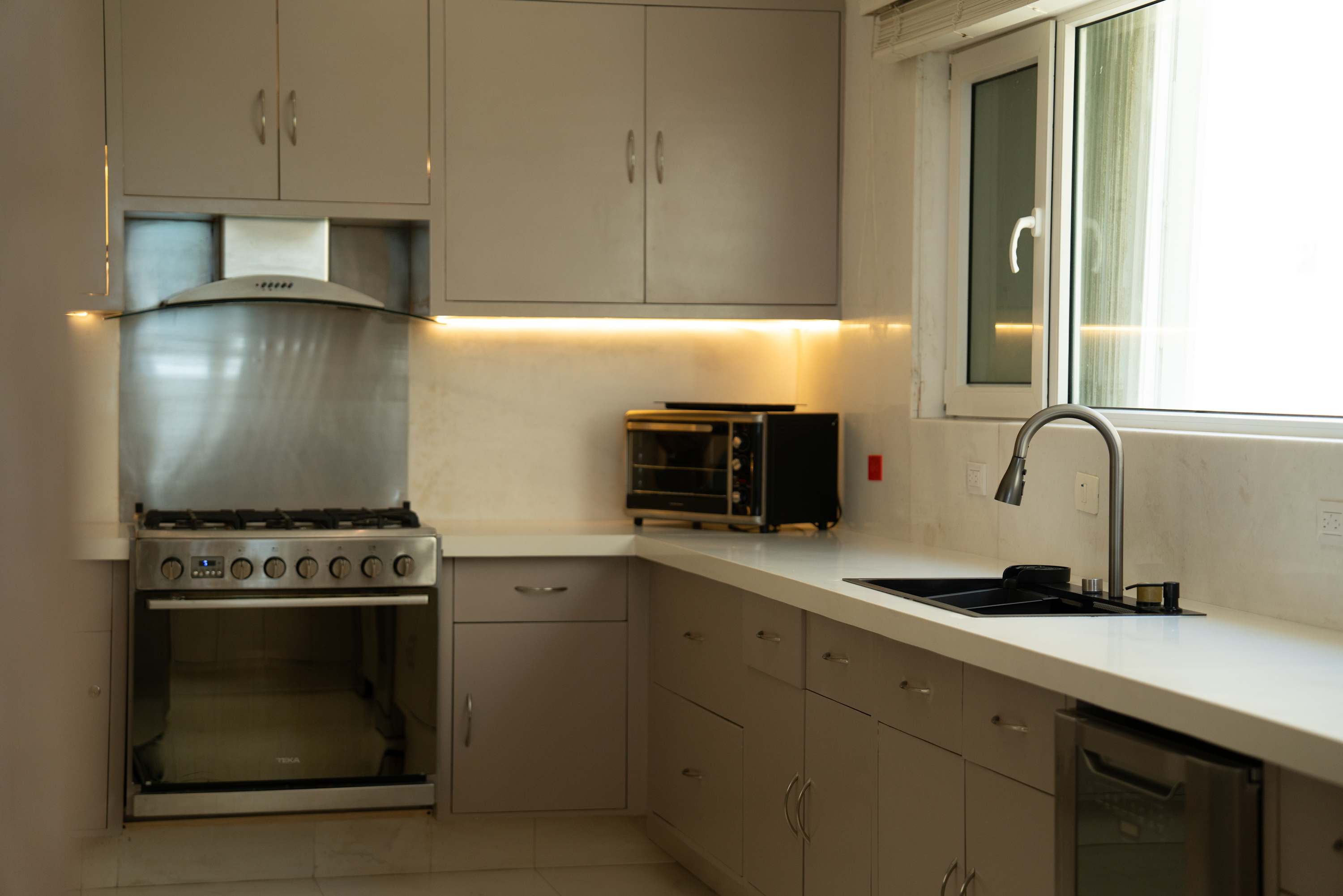 A modern kitchen with grey cabinets, stainless steel appliances, and a white countertop.