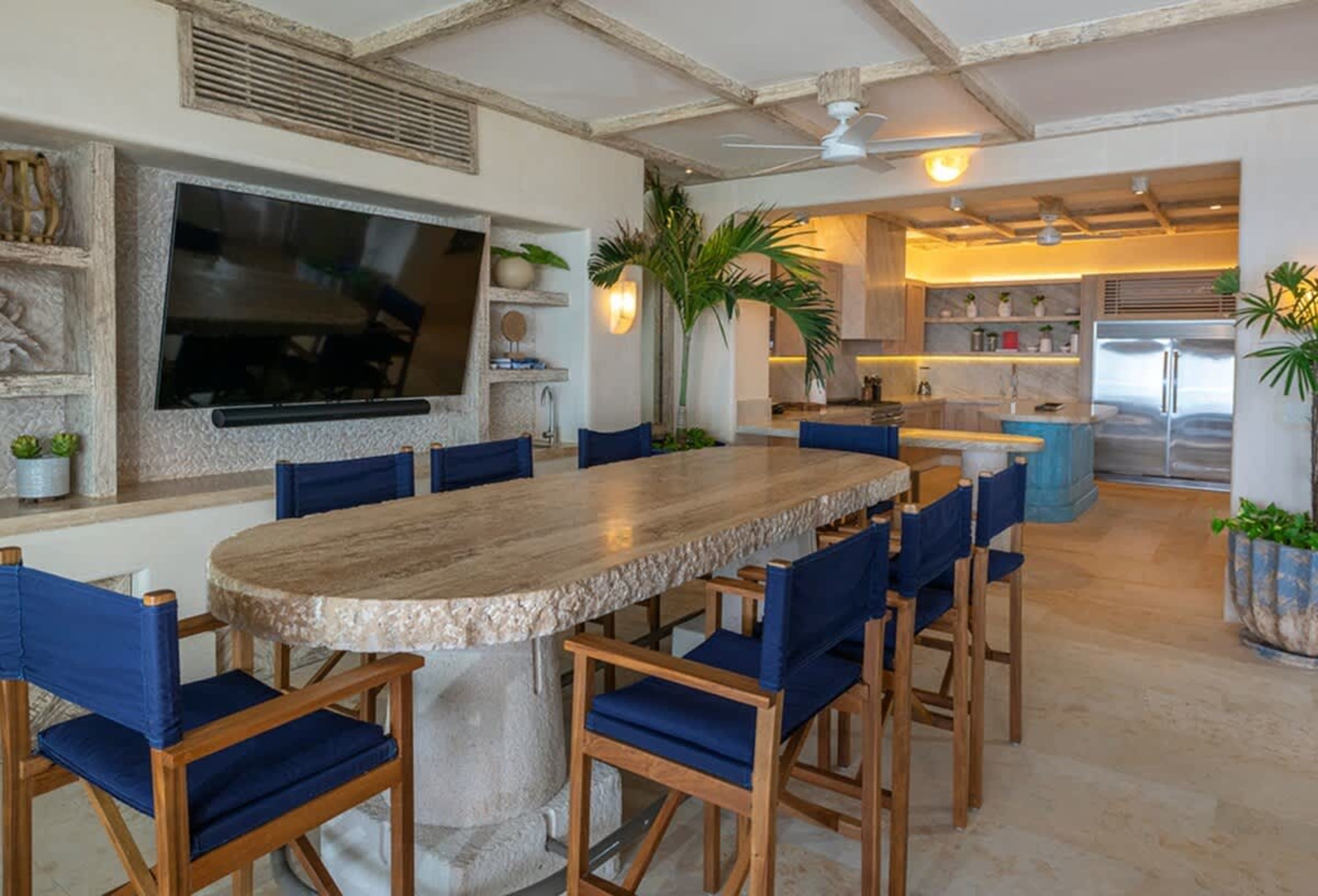 A large, live-edge dining table with chairs sits in a modern, open-concept kitchen with a tv.