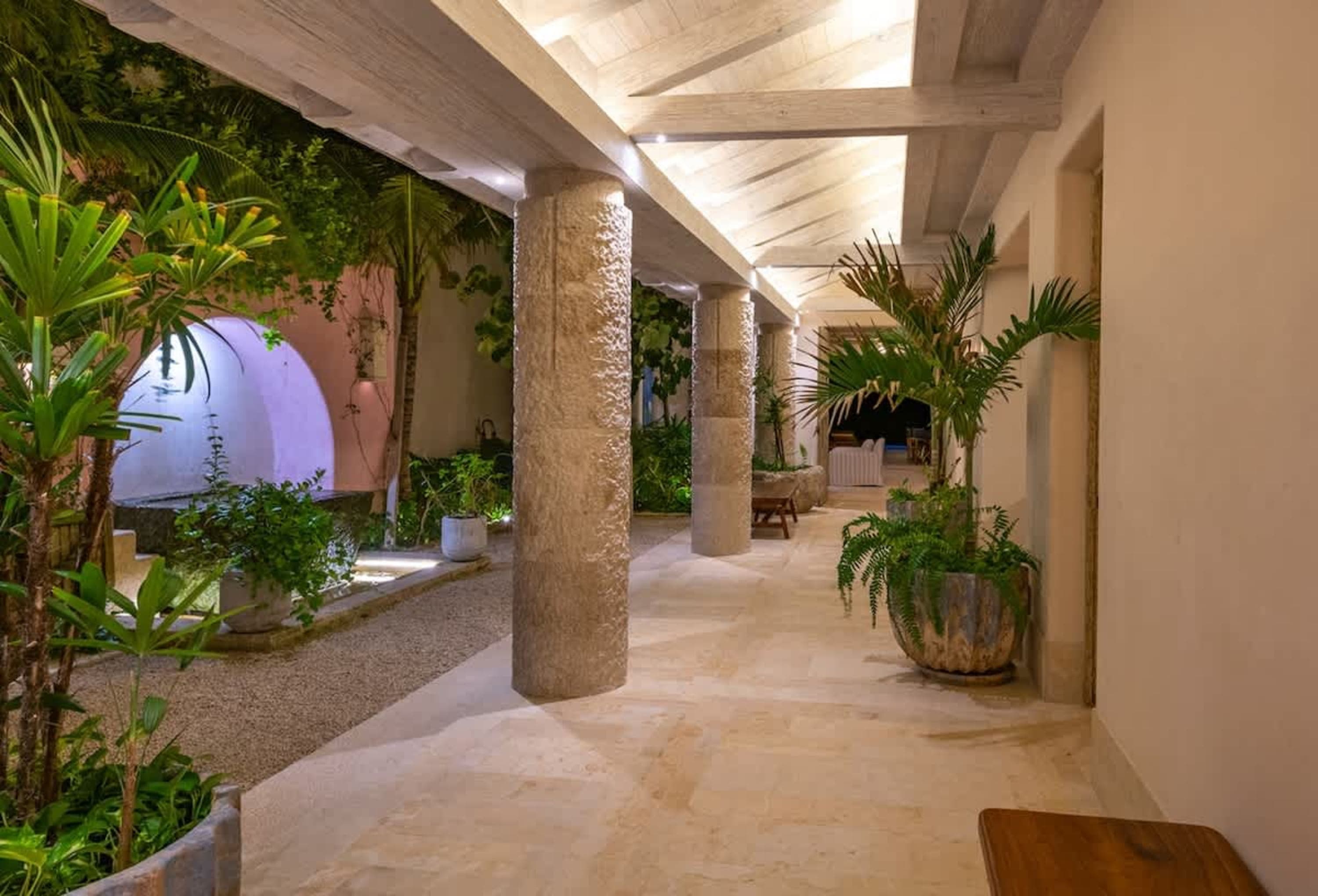 A covered walkway with stone columns and lush greenery.