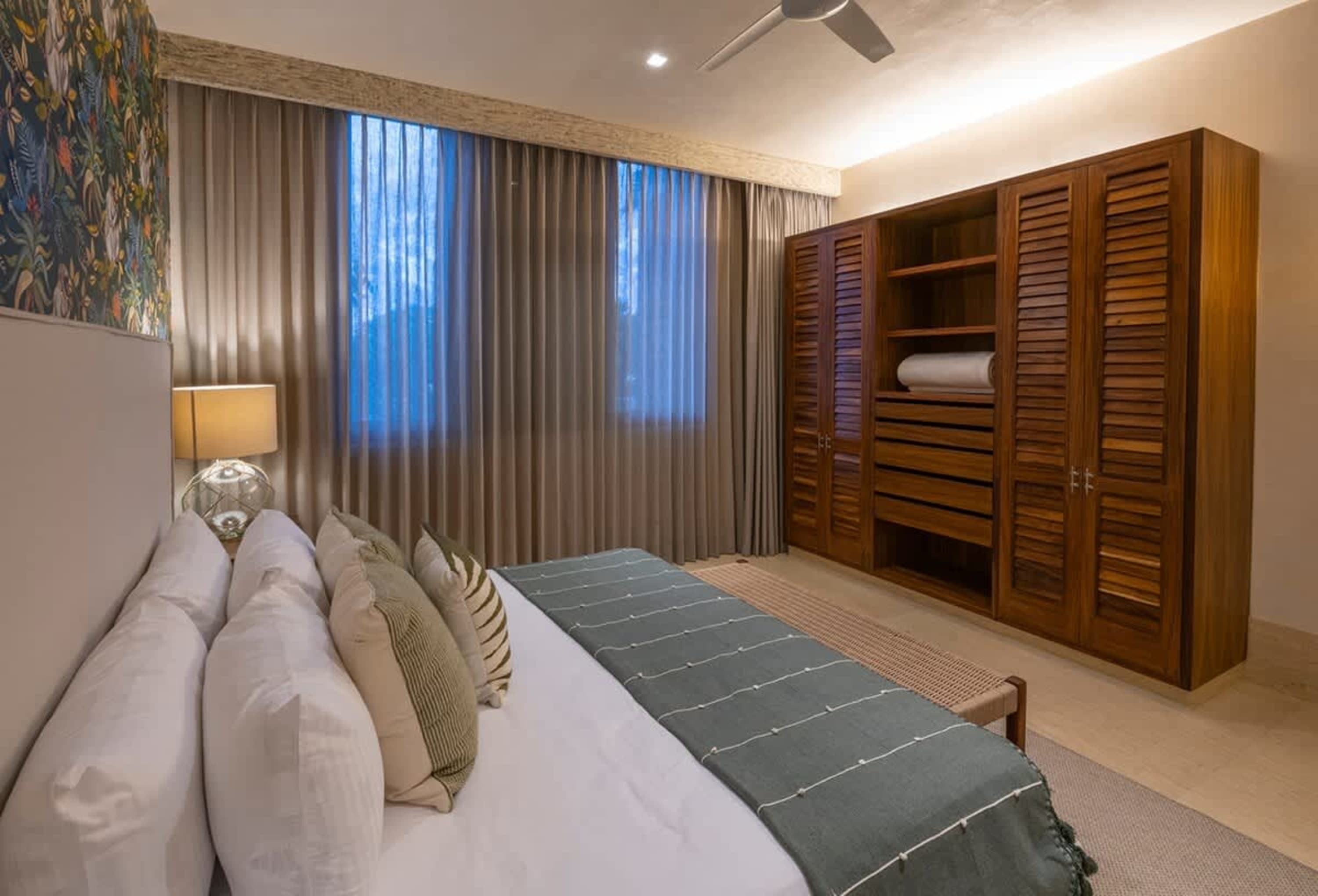 A bedroom with a large wooden wardrobe, a bed with white linens and green accents, and a ceiling fan