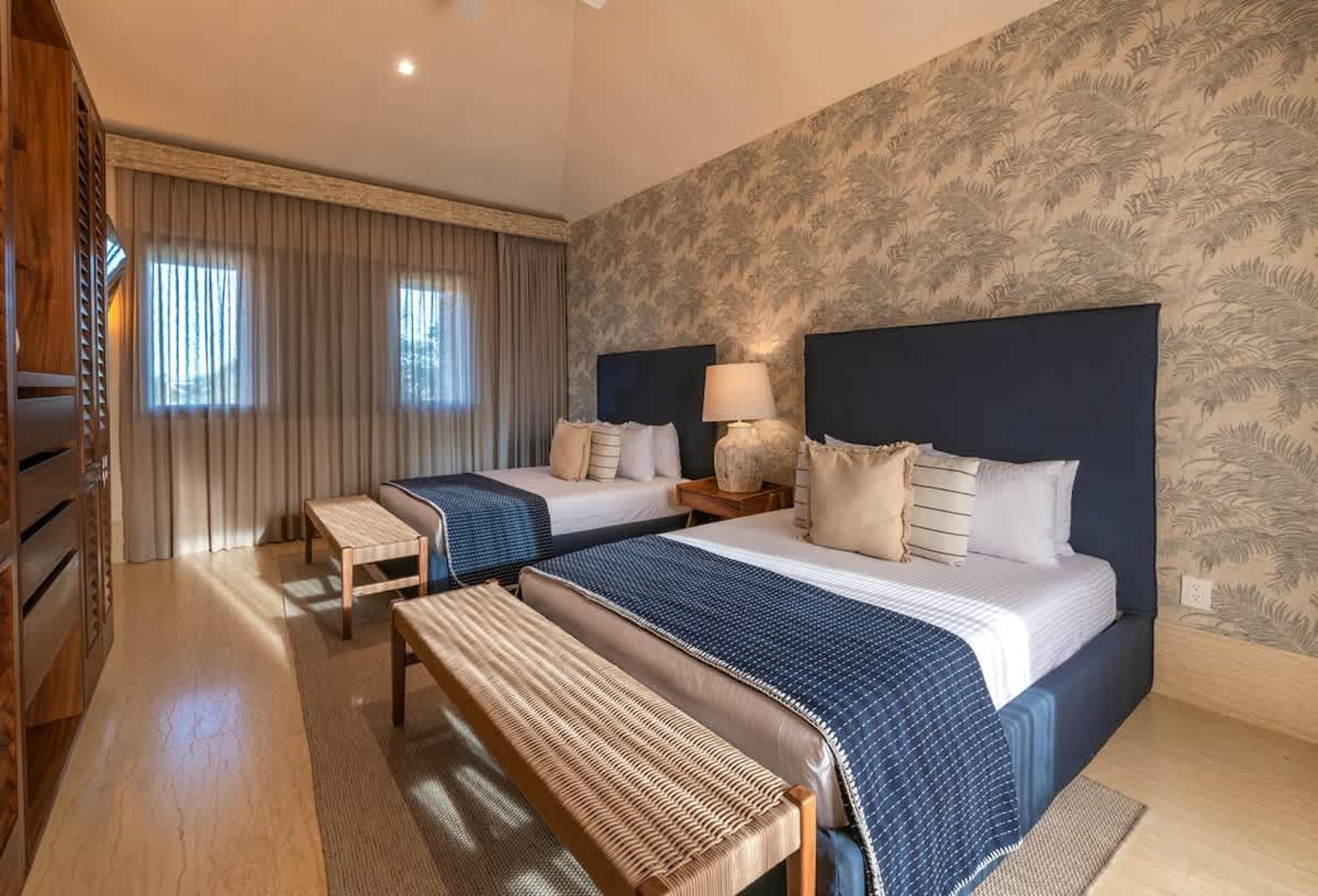Bedroom with two queen beds, dark blue headboards, and nature-themed wallpaper.