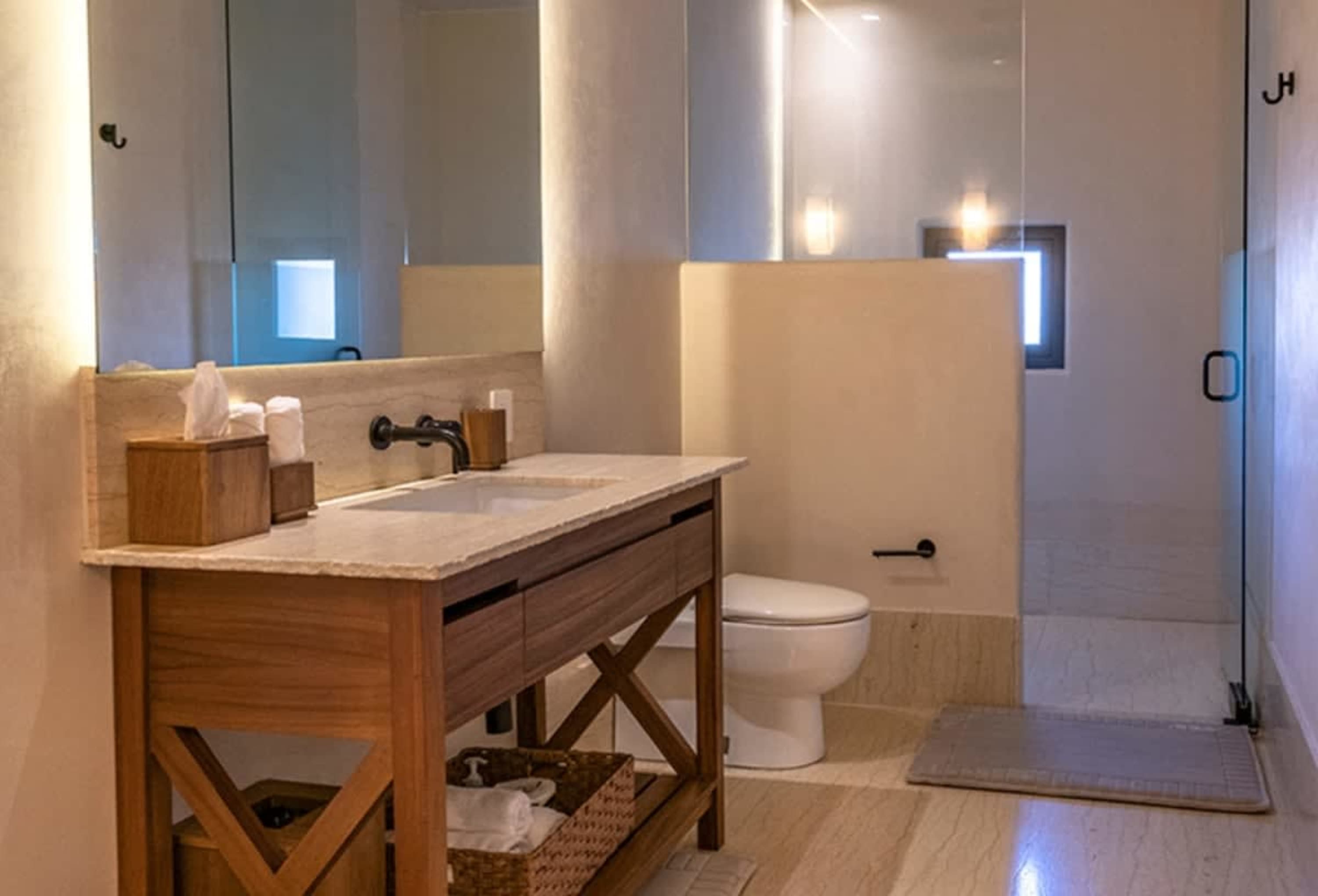 Modern bathroom with wooden vanity, marble countertop, and glass shower enclosure.