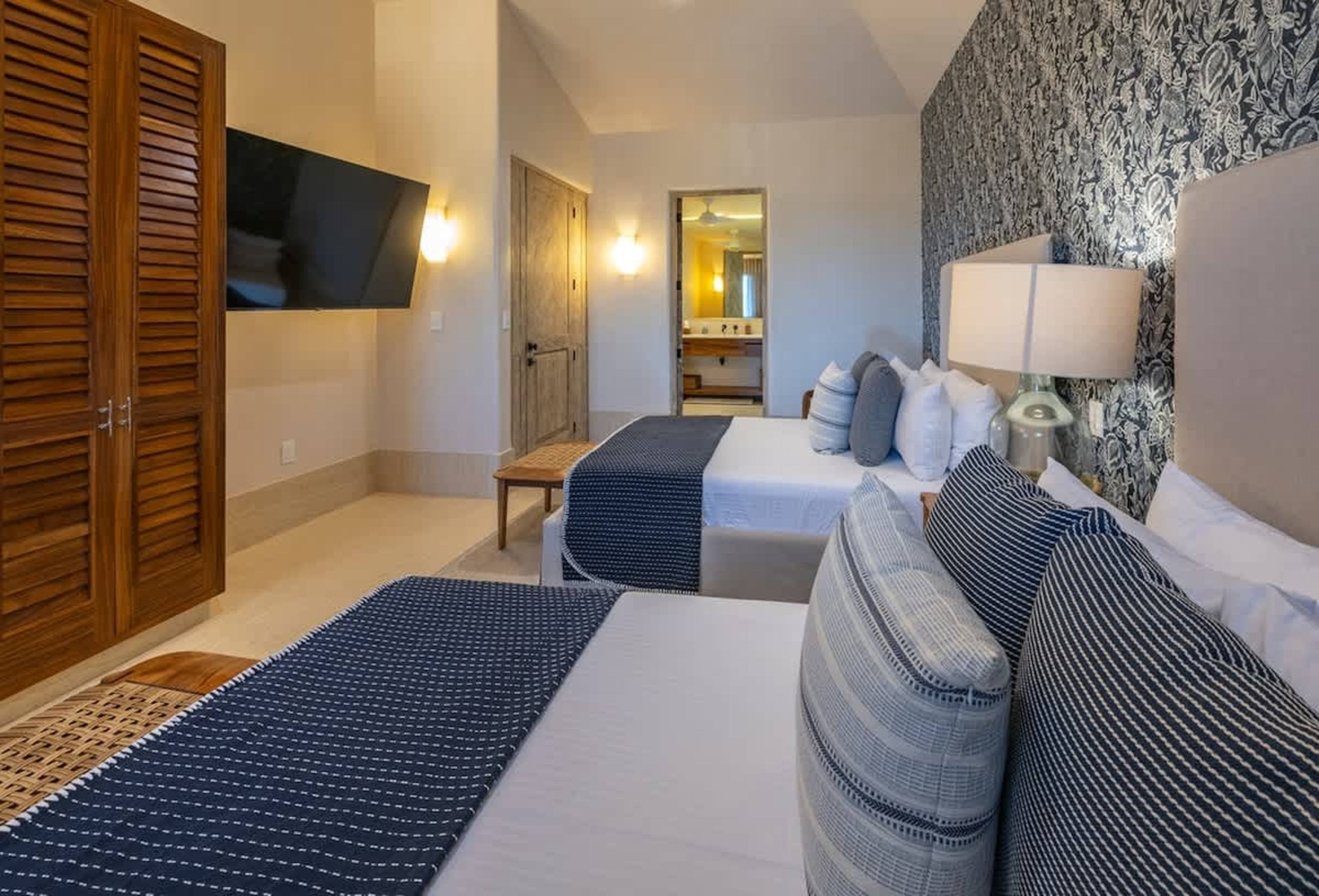 A hotel room with two queen beds, a TV, and a bathroom entrance.
