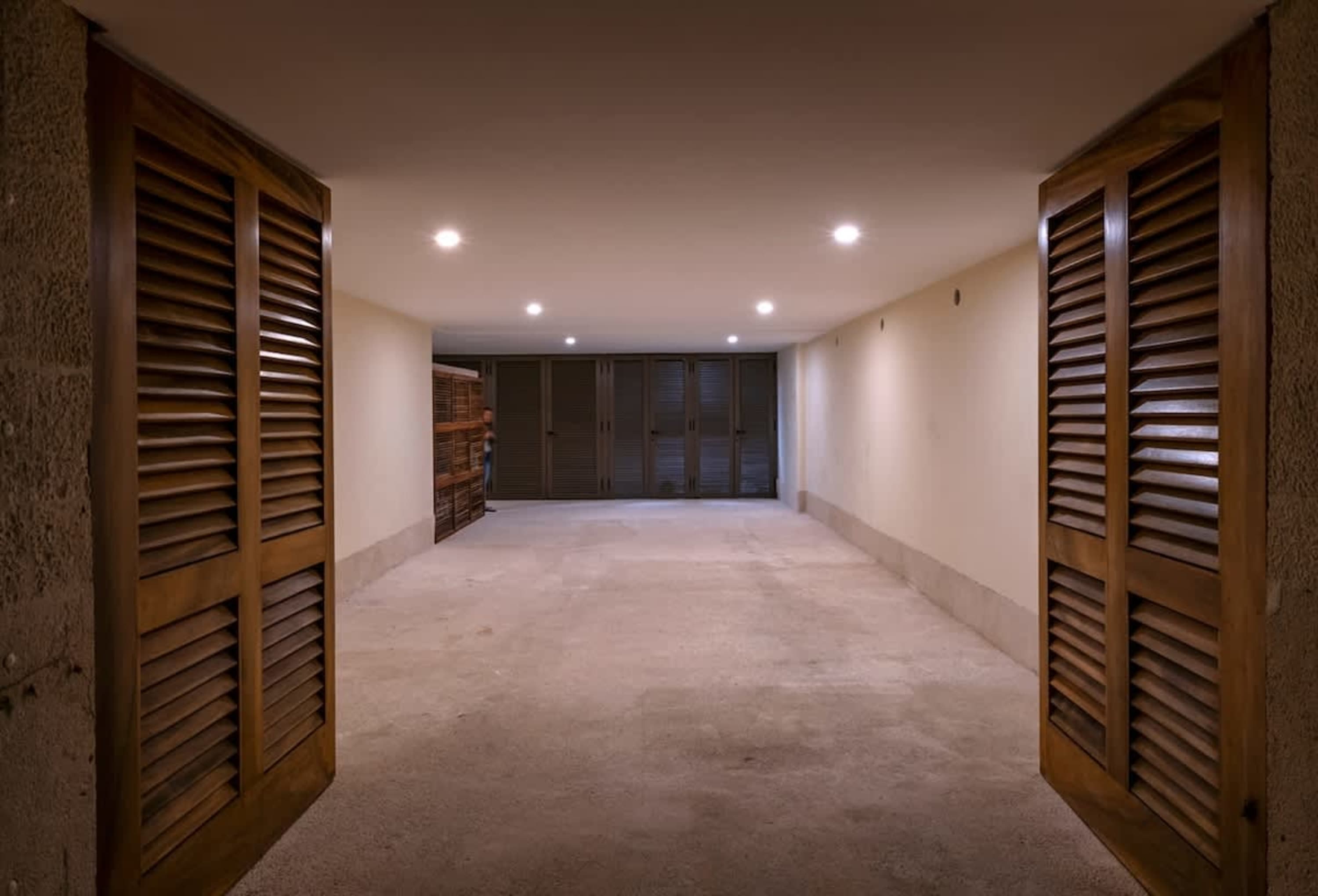A hallway with large wooden doors, concrete floor, and cabinets.