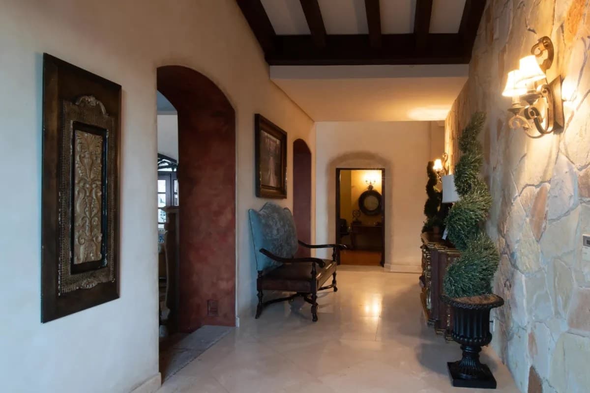 Step into a grand hallway with exposed beams, stone accents, and warm lighting guiding you to elegant living spaces beyond.