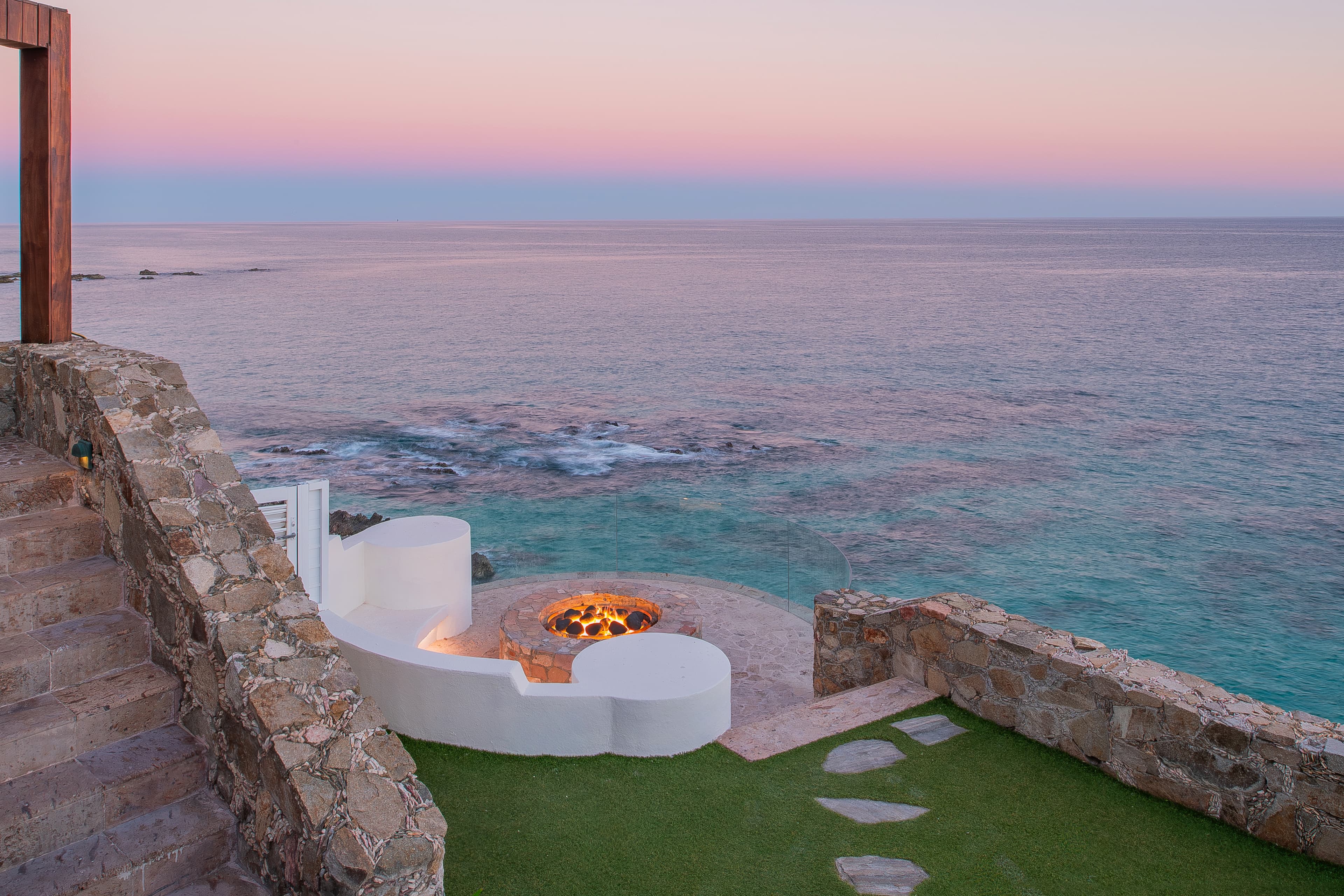This stunning waterfront retreat features a custom fire pit overlooking serene turquoise waters, perfect for unwinding during sunset and experiencing coastal tranquility.