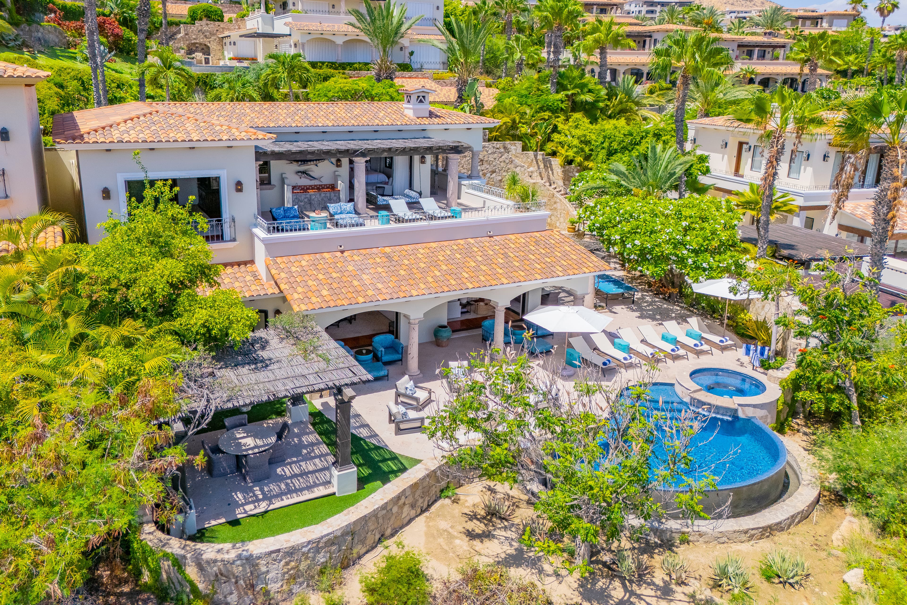 Aerial view of an elegant Mediterranean-style villa featuring private pool, hot tub, multiple terraces, and lush tropical landscaping in a hillside resort community.