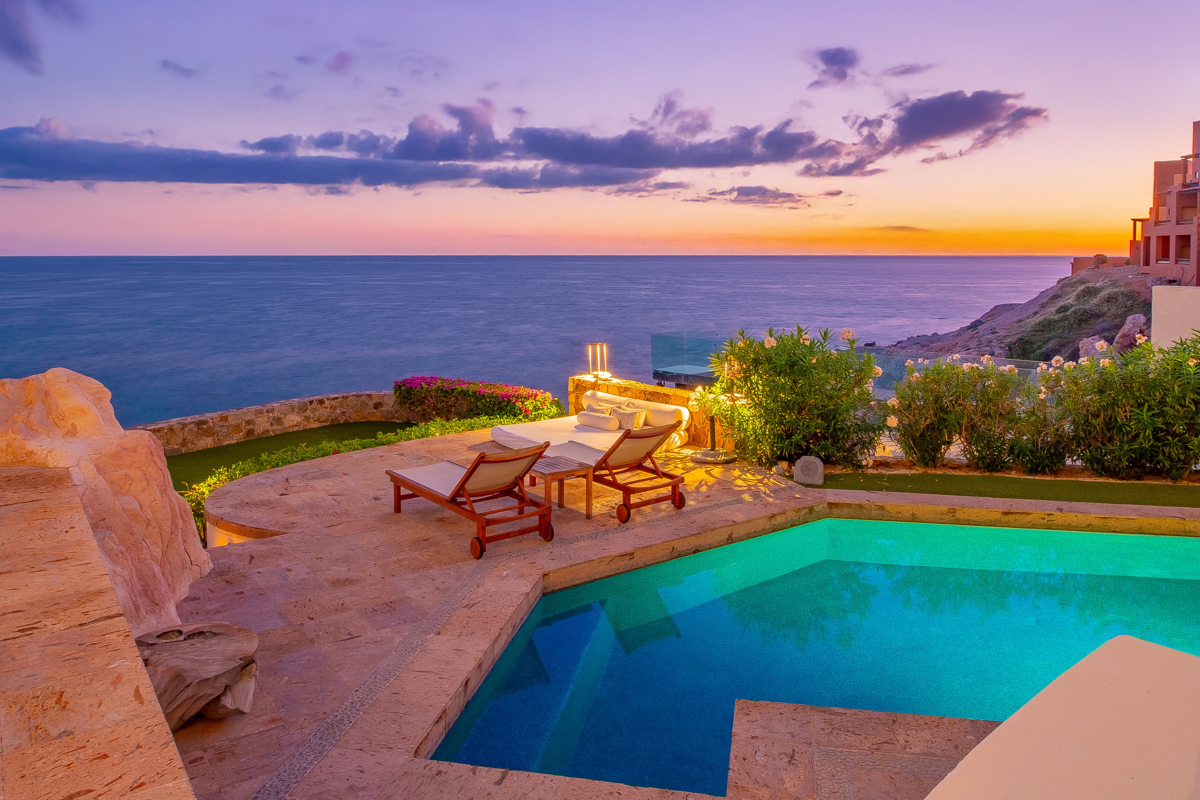 Private pool overlooking the Mediterranean Sea under golden sunset skies, flanked by tropical landscaping and clifftop views that frame the horizon.