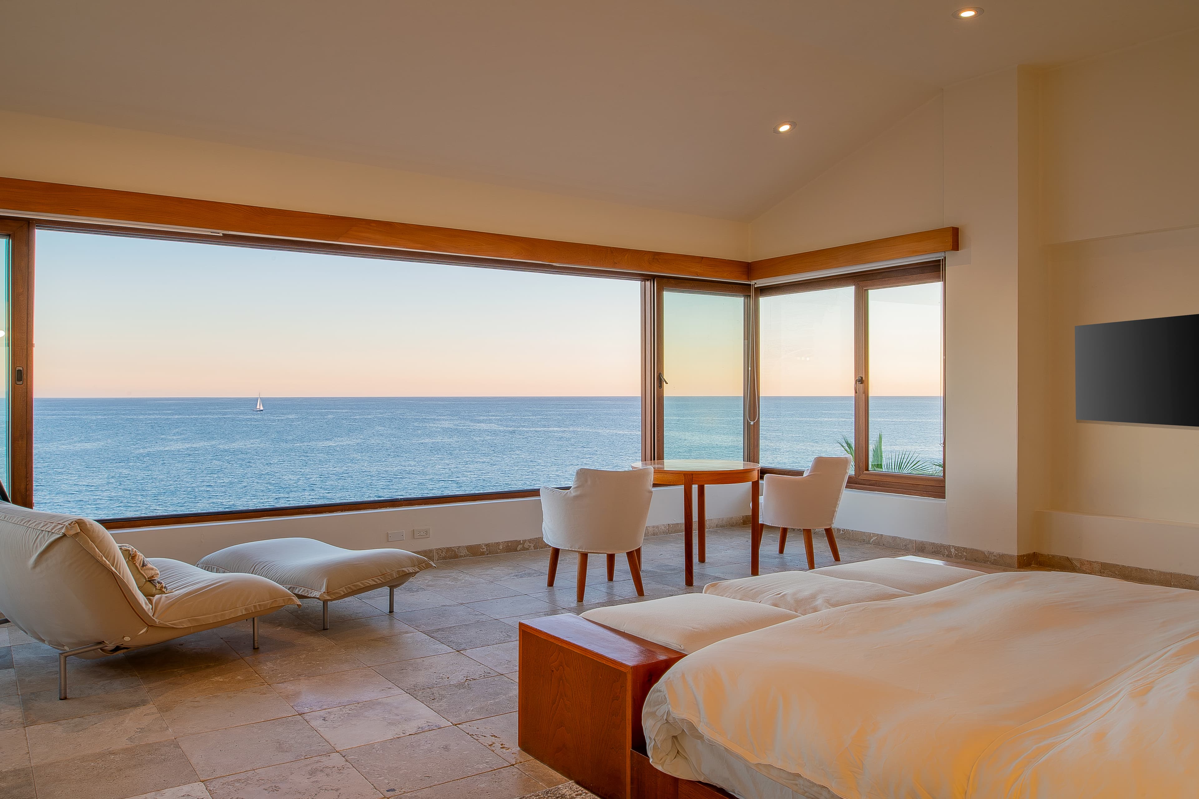 Bedroom 1 (Master) · Drift off to sleep as the gentle sound of waves fills your spacious bedroom, where floor-to-ceiling windows frame endless ocean views and a cozy seating area invites quiet moments.