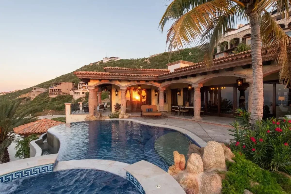 Stunning hillside villa featuring a private pool, spa, and covered terrace with warm ambient lighting as day transitions to evening in a lush coastal setting.
