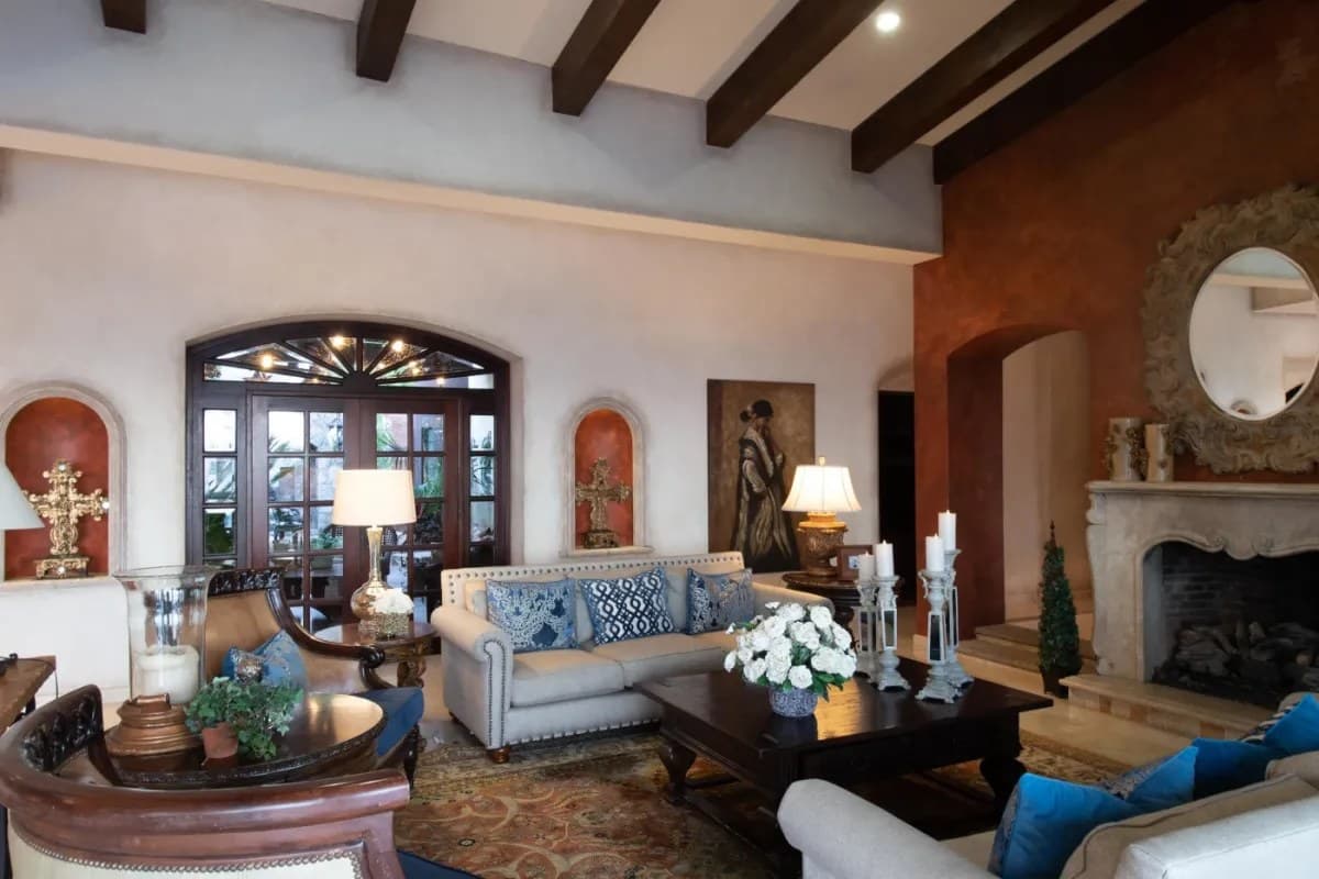 Step into your elegant living room where exposed beam ceilings frame plush seating, a classic fireplace, and graceful architectural details. Unwind amid sophisticated comfort and timeless charm.