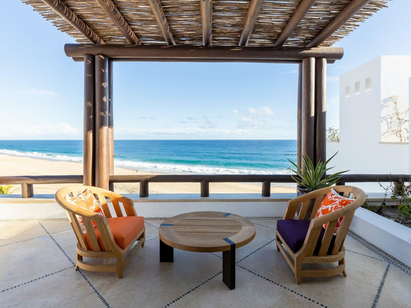 Two chairs and a table below a thatched patio of the home.