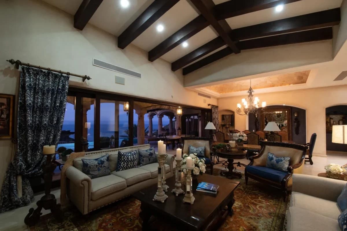 Unwind in your elegant living space with soaring wood-beamed ceilings, plush seating, and stunning ocean views through arched doorways that invite the beauty of the coast inside.