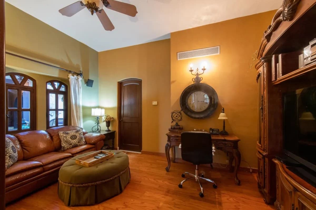 Step into your elegant living space, where warm golden walls, rich leather seating, and beautiful wood furnishings create a welcoming retreat for relaxation or catching up on work.
