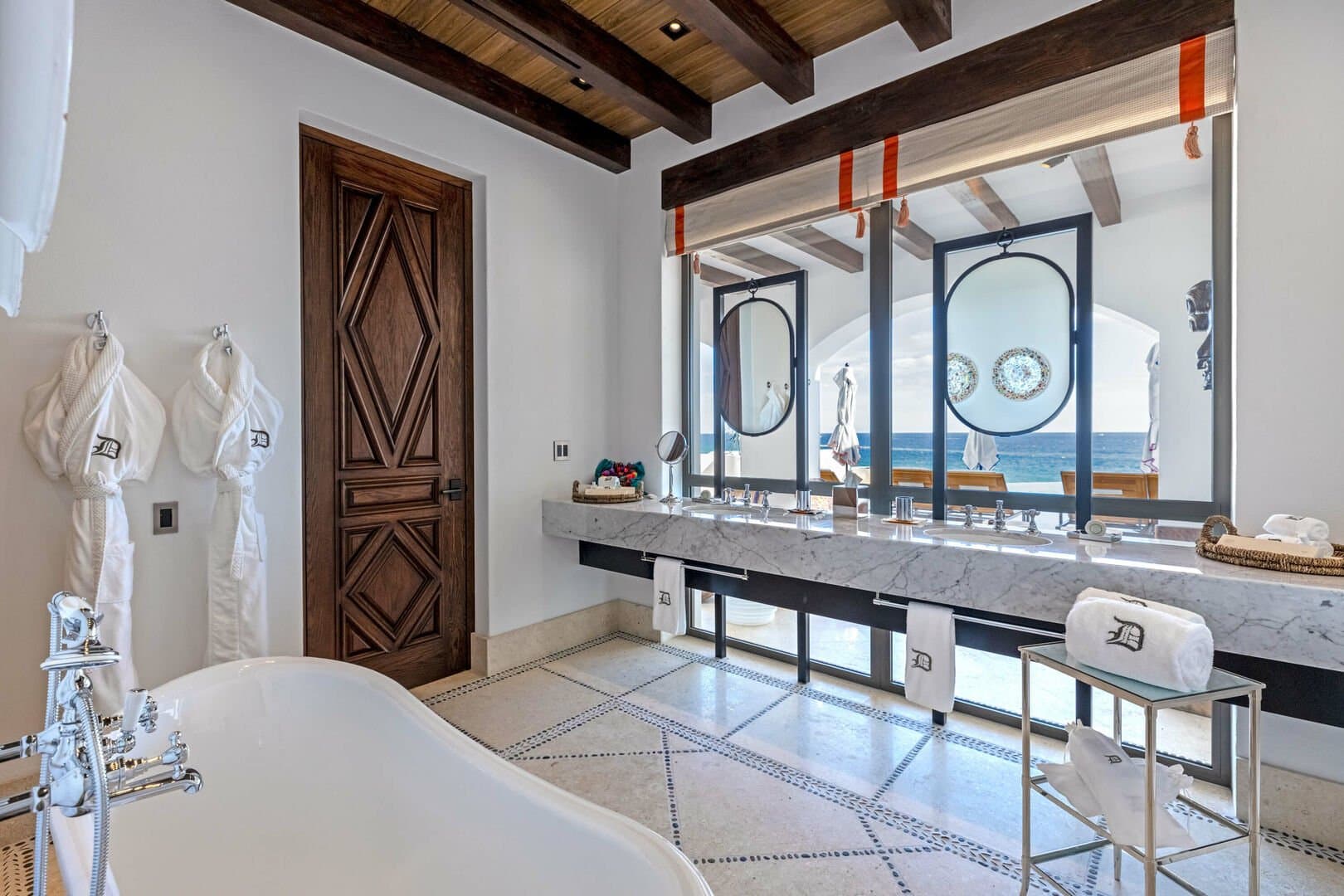 A bathroom with a standing tub and a unique mirror set-up, with mirrors over a large window facing the beach.
