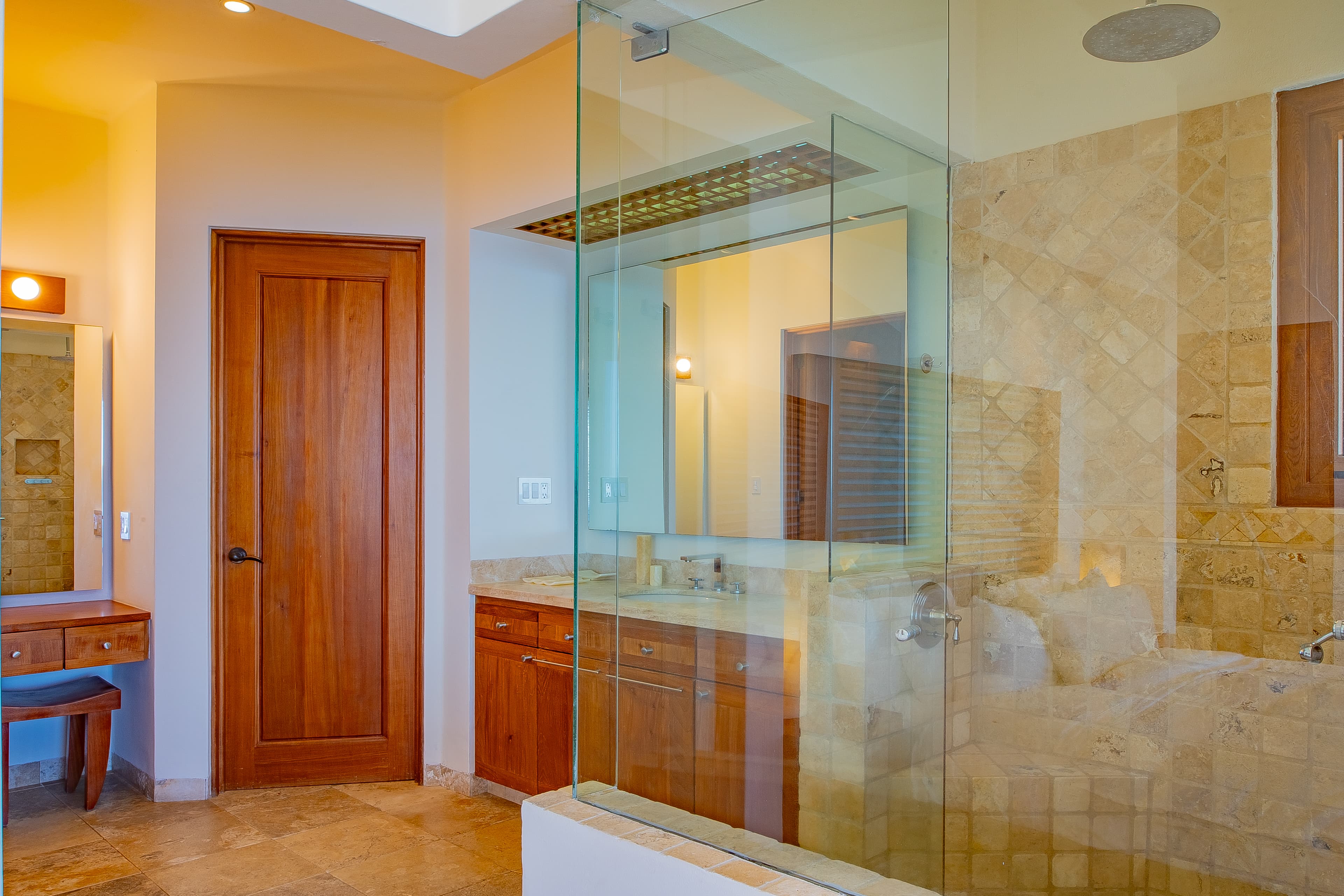 Bathroom 3 · Your private bathroom features elegant travertine tile, a spacious glass-enclosed shower with rainfall showerhead, and warm wood cabinetry for a spa-like retreat.