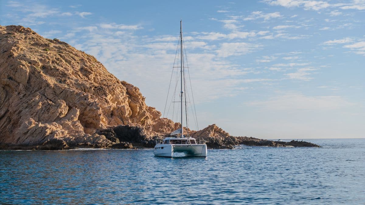 A sailboat anchored in crystal-clear waters near dramatic rocky cliffs creates the perfect coastal escape setting.