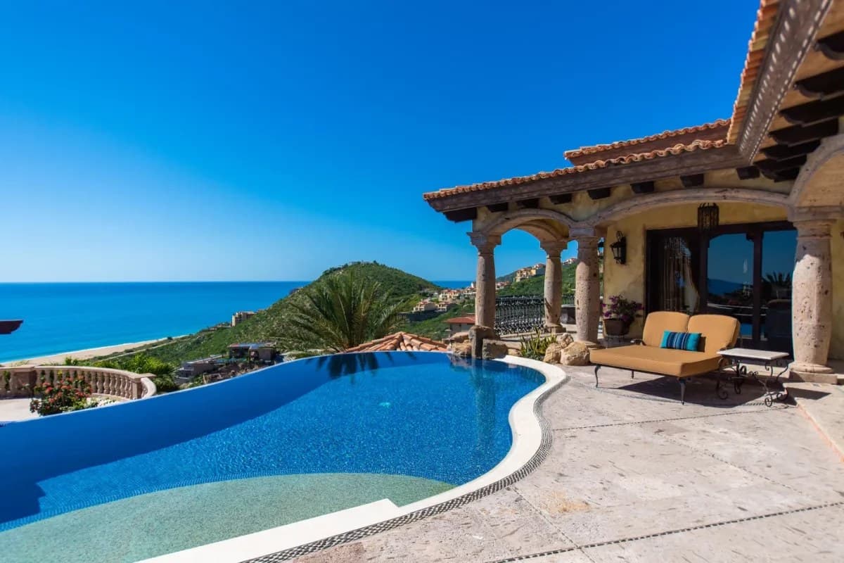 Luxurious infinity pool with breathtaking panoramic views of lush hillsides and the sparkling azure sea, surrounded by elegant Mediterranean-style architecture and comfortable outdoor lounging spaces.
