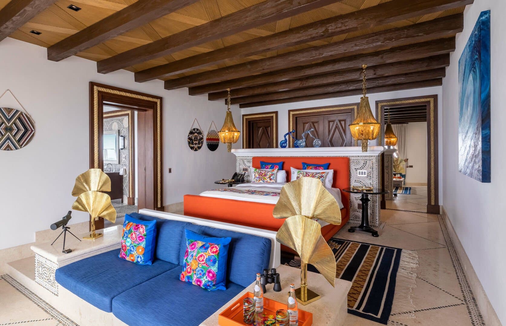 A bedroom of this Los Cabos beachfront villa, with an orange bed and a blue couch in front of it.