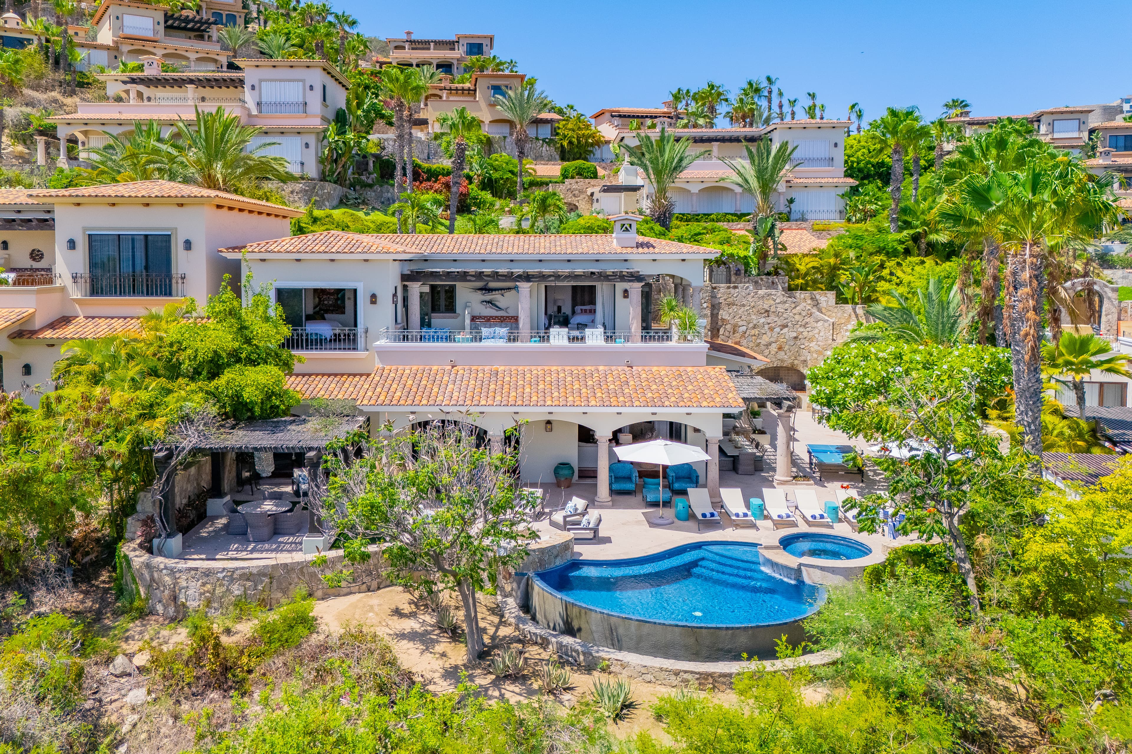 Hillside luxury villa surrounded by lush tropical landscaping with pool, hot tub, and multiple terraces overlooking a prestigious coastal residential neighborhood.