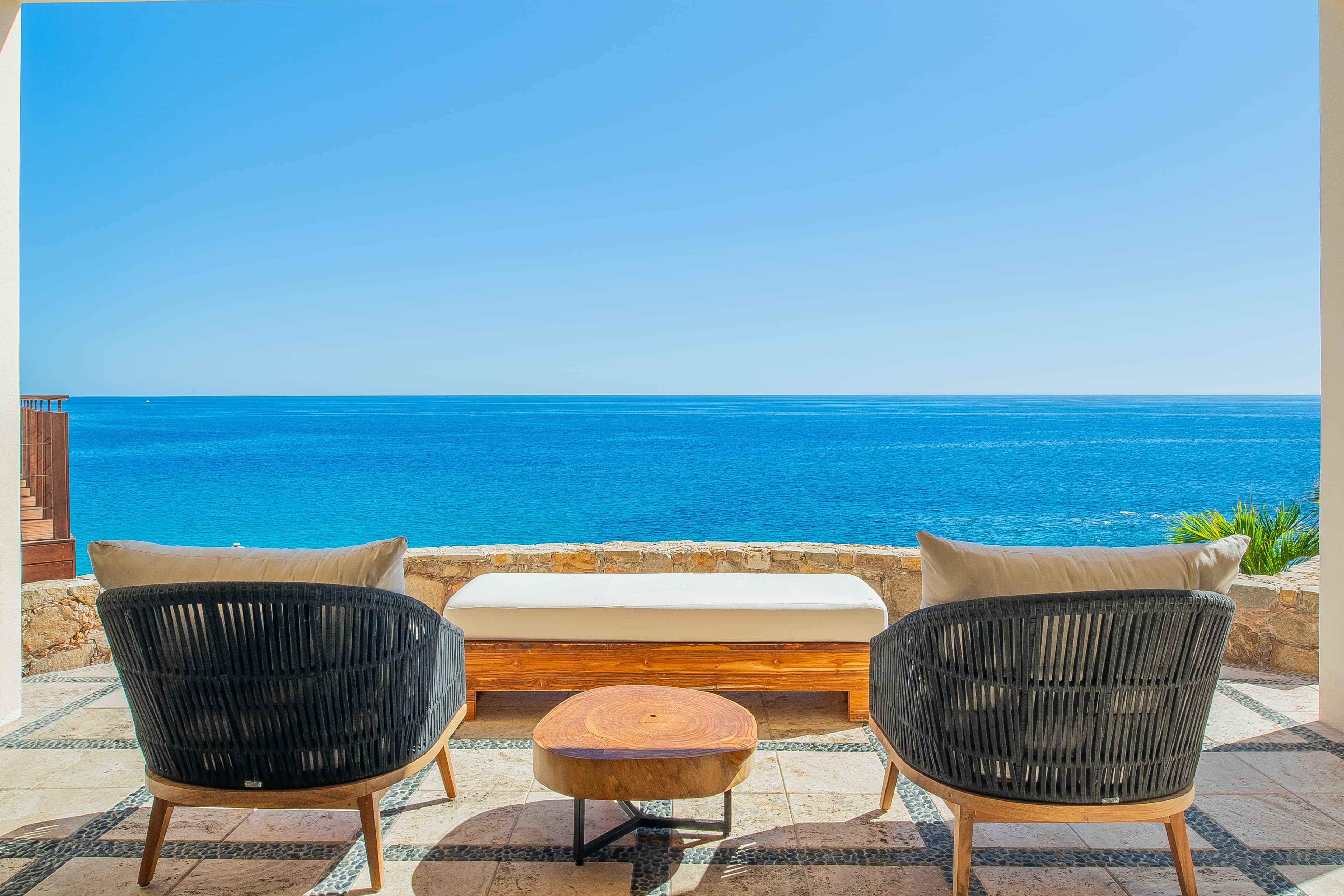 This private terrace overlooking the turquoise sea offers an ideal spot for morning coffee or evening relaxation. Stone walls frame endless ocean views under brilliant blue skies.