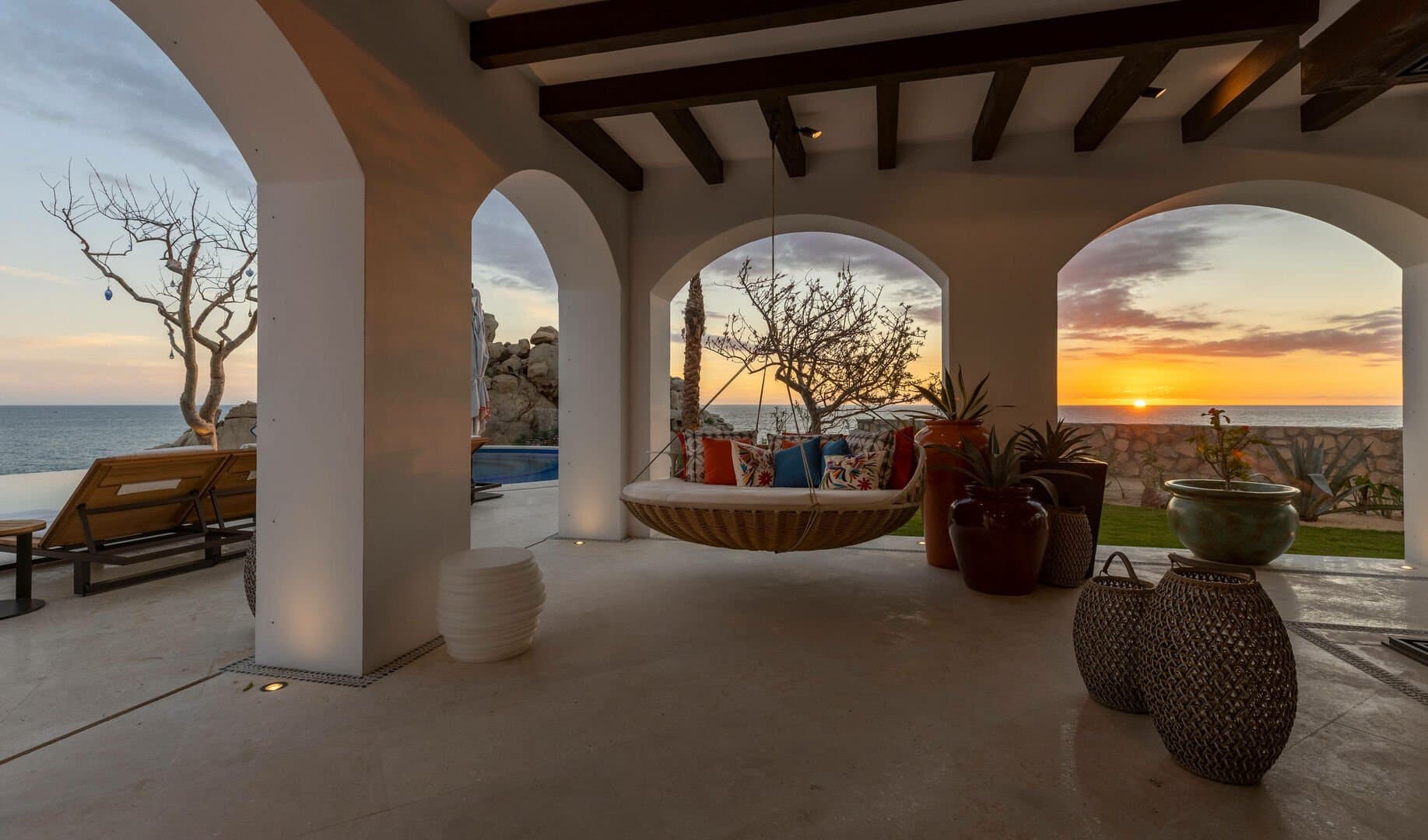 A hammock hanging from the ceiling beams of a patio at sunset.