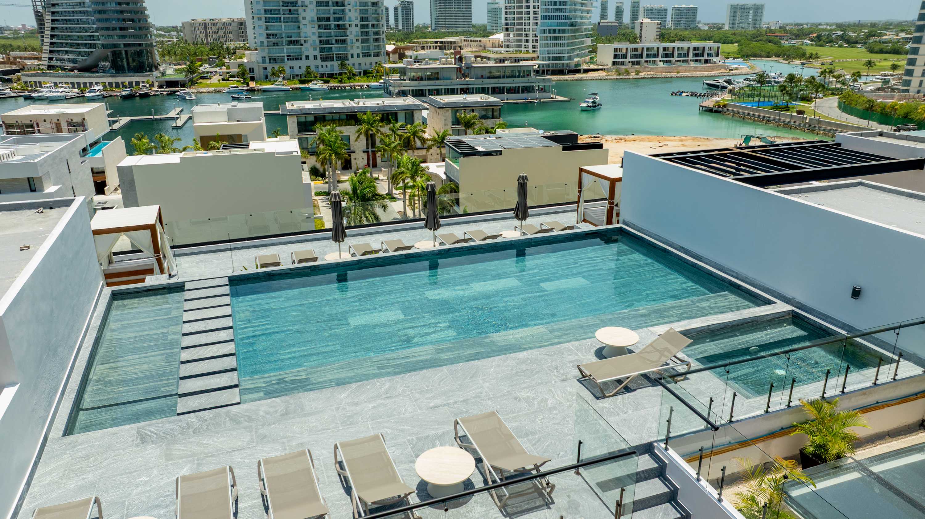 Rooftop pool with lounge chairs and umbrellas, overlooking a marina and city skyline.