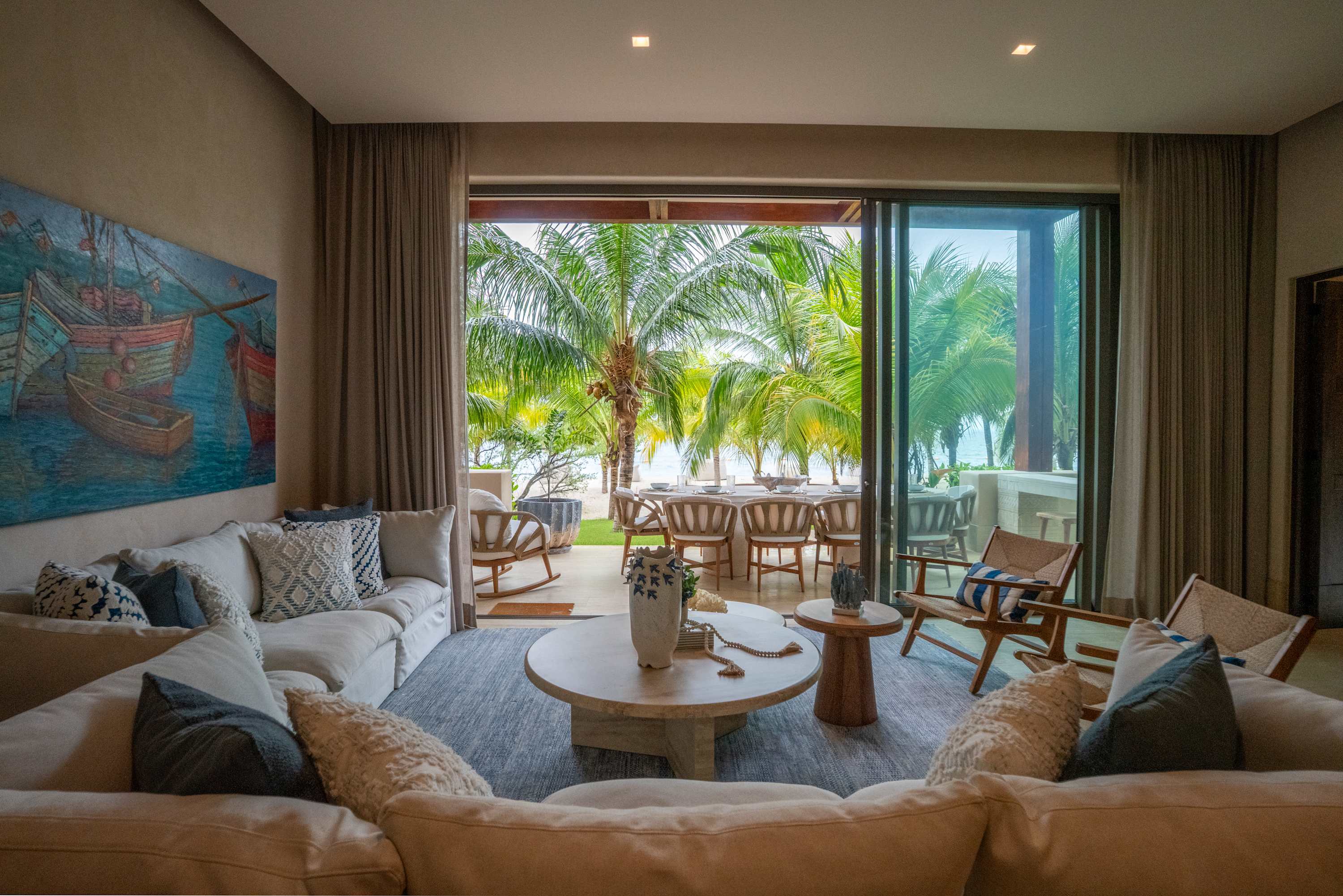 Living room with a large couch, coffee table, and a view of palm trees and the ocean.