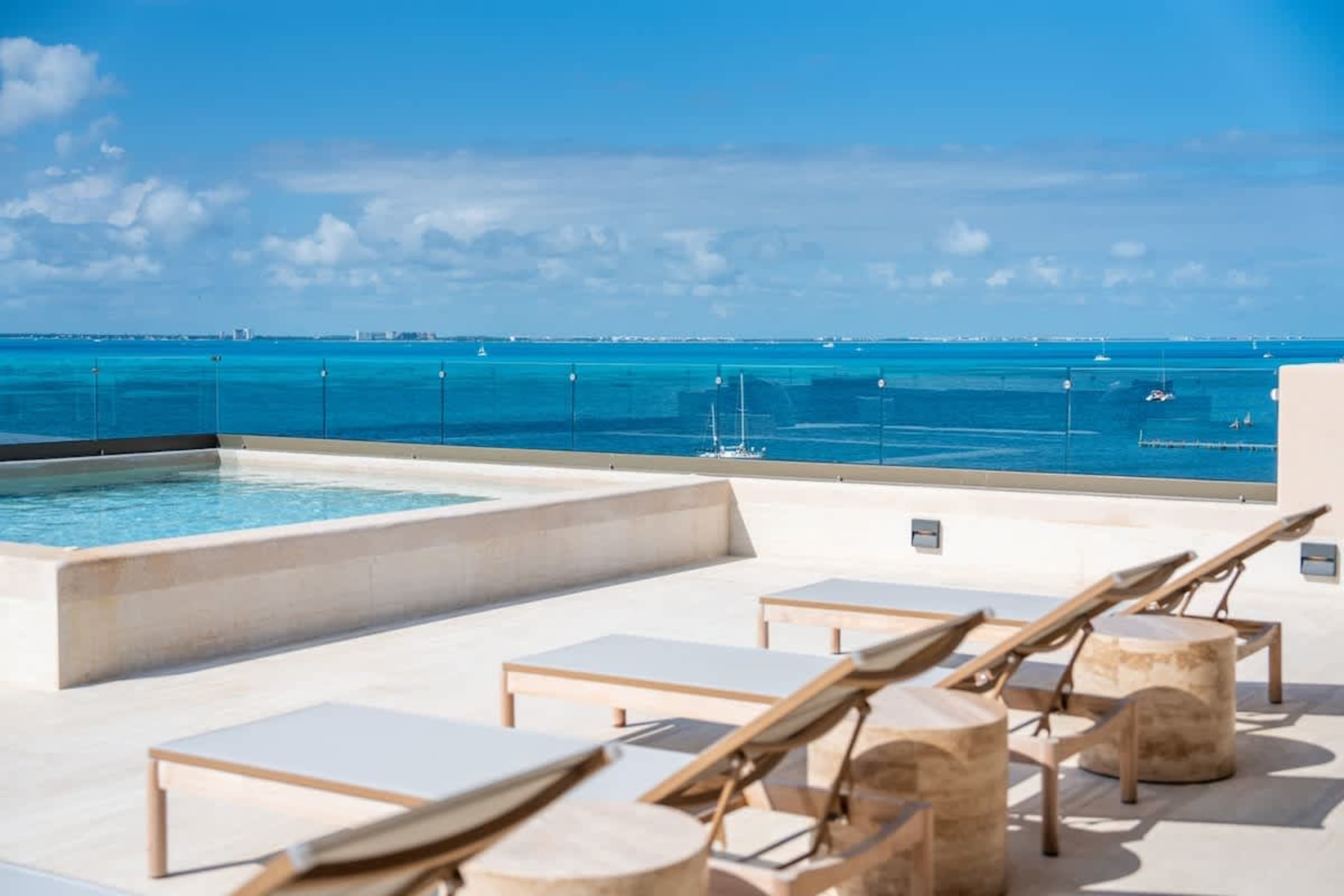 Rooftop pool with lounge chairs overlooking the turquoise ocean and a cityscape.